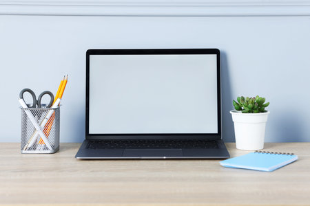 Laptop, stationery and floral decor on wooden office table near light wall