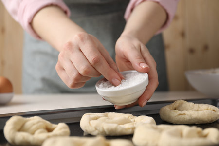 Woman putting salt onto raw pretzels at white table, closeupの写真素材
