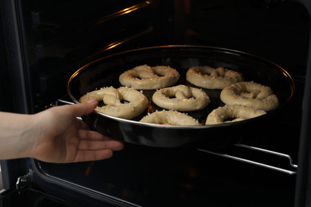 Woman putting baking dish with uncooked pretzels into oven, closeup