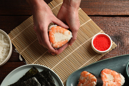 Woman holding onigiri (Japanese rice ball) with shrimp at wooden table, top viewの写真素材