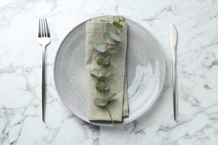 Stylish plate, napkin, cutlery and eucalyptus branch on white marble table, flat layの写真素材