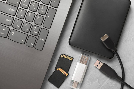 Flash drive, SD memory cards, external hard disk and laptop on gray textured table, flat lay