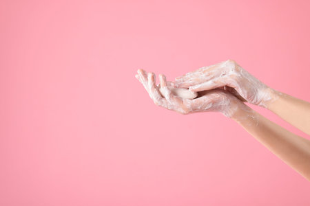 Woman washing hands with soap on light pink background, closeup. Space for text
