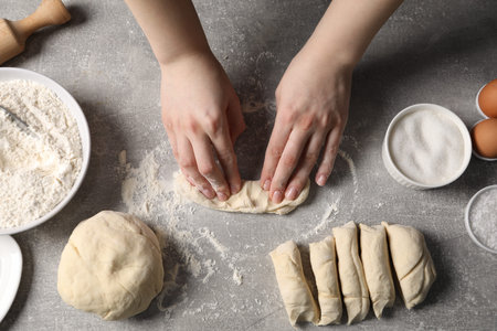 Woman kneading raw dough at light grey table, top view