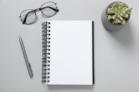 Open blank notebook, glasses, pen and floral decor on light grey background, flat layの写真素材