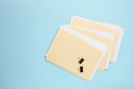 File folders with papers and binder clips on light blue background, flat lay. Space for text