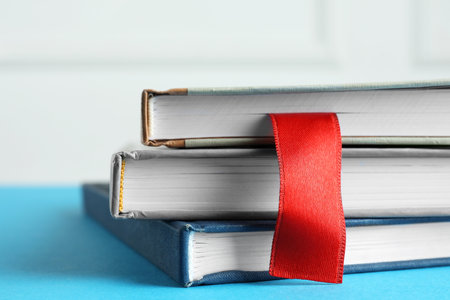 Book with red ribbon bookmark and colorful ones on blue table against light background, closeupの写真素材