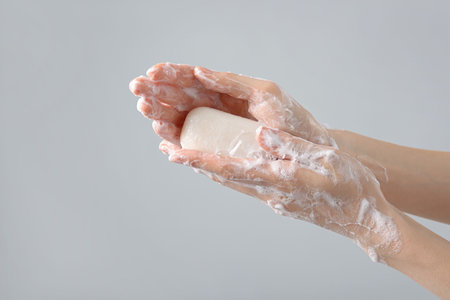 Woman washing hands with soap on light grey background, closeup