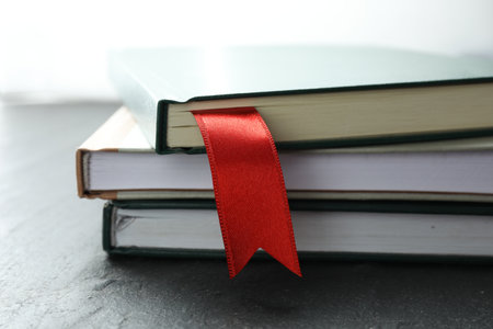 Book with red ribbon bookmark and colorful ones on grey textured table, closeupの写真素材