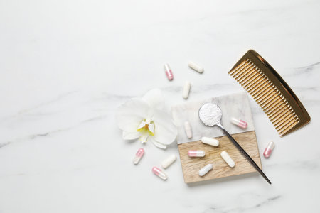 Collagen capsules, powder, comb and flower on white marble table, flat lay. Space for textの写真素材