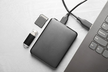 External hard disk connected to laptop, SD memory card and flash drive on gray textured table, flat...