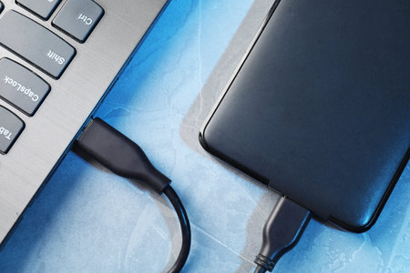 Hard disk drive with USB cable connected to laptop on blue textured table, top view