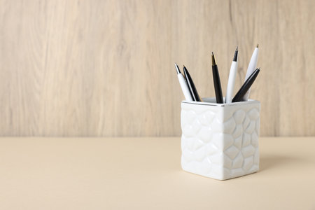 Ballpoint pens in holder on beige table against wooden background. Space for textの写真素材
