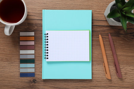 Pens, notebooks, colorful stickers, tea and floral decor on wooden table, flat lay