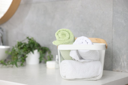 Clean towels in basket, cosmetic products and houseplant on vanity indoorsの写真素材