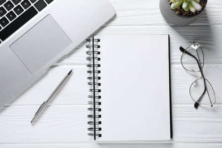 Pen, open notebook, glasses, floral decor and laptop on white wooden table, flat layの写真素材