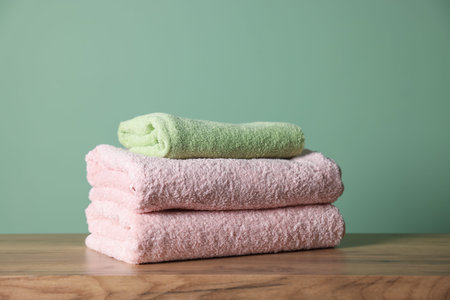 Stack of clean towels on wooden table against green background, closeupの写真素材