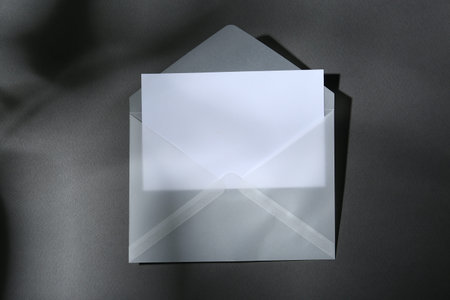 Blank greeting card in paper envelope on dark grey background, top view