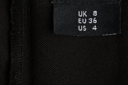 Clothing label on black garment as background, closeup