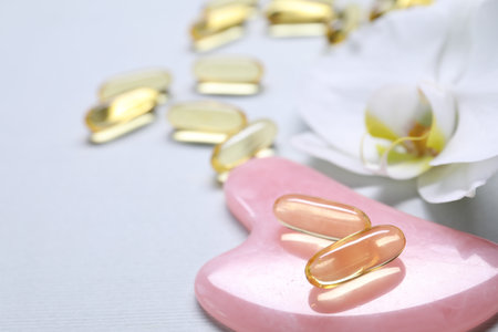 Collagen capsules, gua sha and flower on white background, closeup. Space for textの写真素材