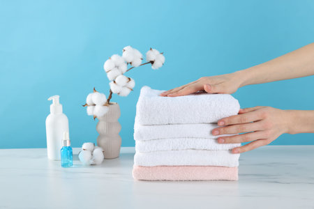 Woman stacking clean towels at white marble table against light blue background, closeupの写真素材