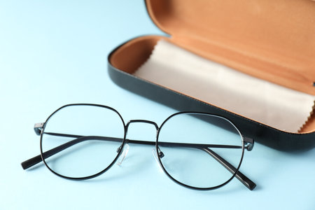 Case with stylish glasses and cleaning cloth on light blue background, closeupの写真素材