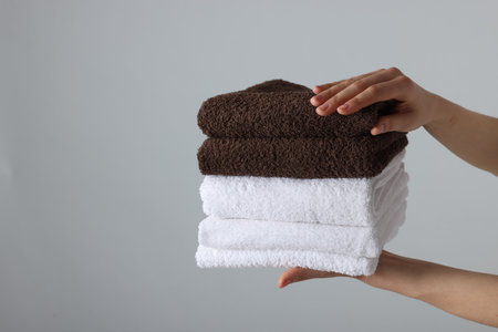 Woman holding stack of clean towels on light background, closeup. Space for textの写真素材