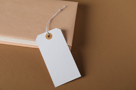 Blank tag with string and book on brown background, closeup. Space for text