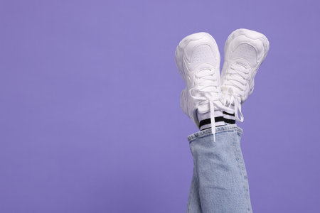 Woman wearing stylish sneakers on purple background, closeup. Space for textの写真素材