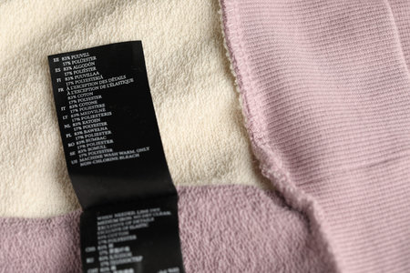Clothing label with material content on color garment as background, above view