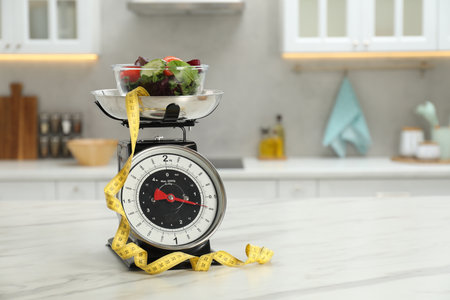 Kitchen scales with salad and measuring tape on light marble table indoors, space for textの写真素材
