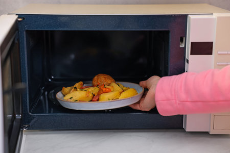 Woman putting plate with lunch into microwave indoors, closeupの写真素材