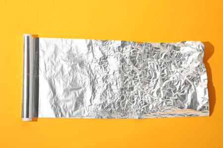Roll of aluminum foil on yellow background, top viewの写真素材