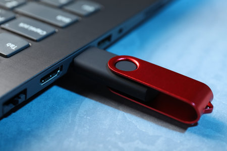 Usb flash drive connected to laptop on blue textured table, closeup