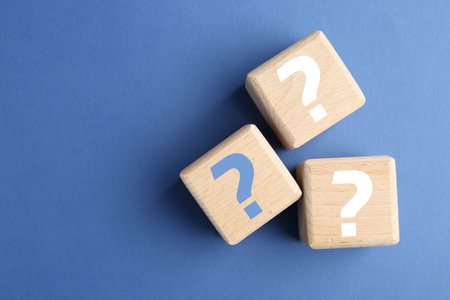 Wooden cubes with question marks on blue background, top view. Space for text