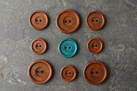 Individuality, uniqueness, different. Turquoise sewing button among brown ones on grey textured...