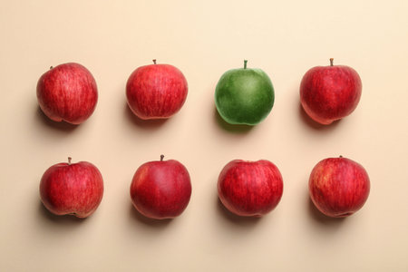 Green apple among red ones on beige background, flat lay