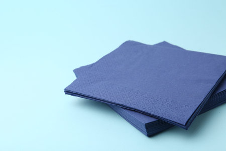 Stack of disposable paper handkerchiefs on light blue background, closeup. Space for text
