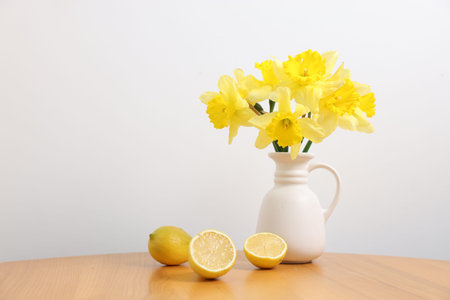 Beautiful daffodils in vase and lemons on wooden table near white wall at homeの写真素材