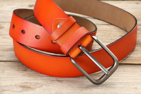 One orange leather belt on wooden table, closeup