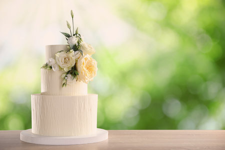 Beautiful wedding cake with floral decor on wooden table outdoors. Space for textの写真素材