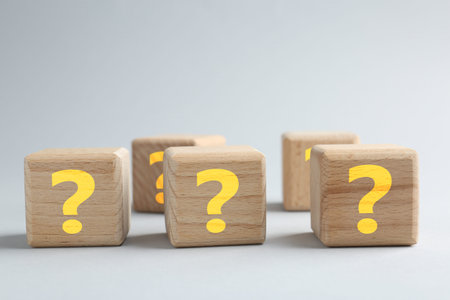 Wooden cubes with question marks on light grey background, closeup