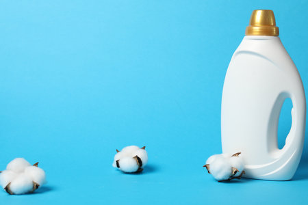 Bottle of fabric softener and cotton flowers on light blue background, space for textの写真素材