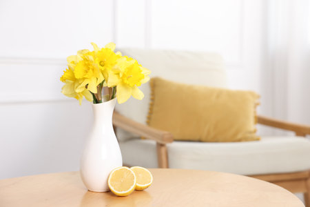Beautiful daffodils in vase and lemons on wooden table at home. Space for textの写真素材