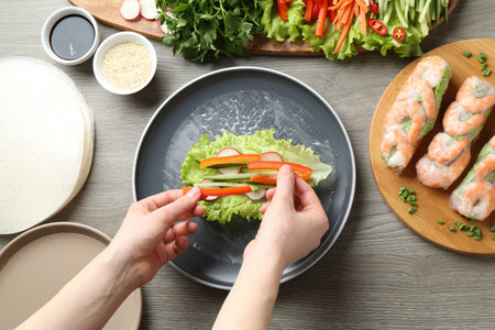 Woman making tasty spring roll at grey wooden table, top viewの写真素材
