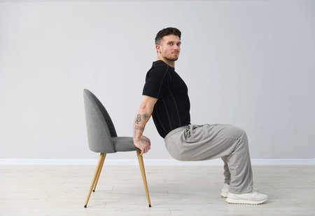 Handsome man exercising with chair at home
