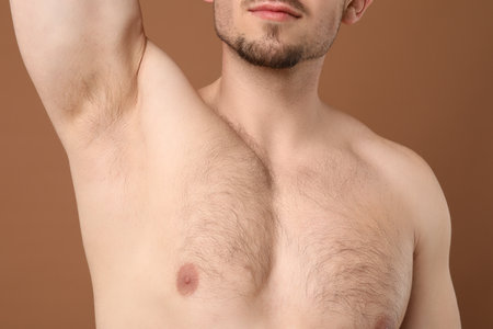Young man showing hairy armpit on brown background, closeup. Epilation procedureの写真素材