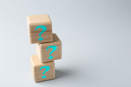 Stack of wooden cubes with question marks on light grey background, space for textの写真素材