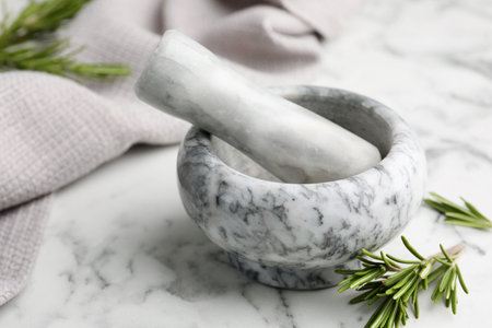 Mortar with rosemary, pestle and cloth on white marble table, closeupの写真素材