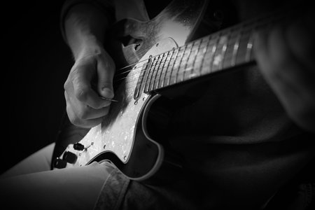 Man playing guitar in darkness, closeup. Black and white effect